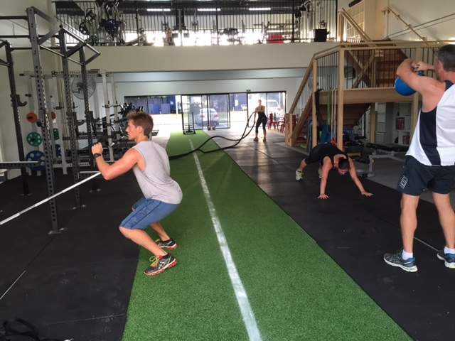 Seseorang sedang melakukan latihan beban atau strength training di dalam pusat kebugaran dengan menggunakan barbel untuk melatih kekuatan otot.
