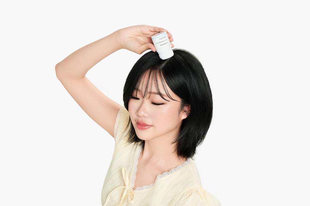 Seorang wanita sedang menyemprotkan dry shampoo ke pangkal rambutnya untuk menerapkan tren lazy hairscaping agar bebas dari lepek.